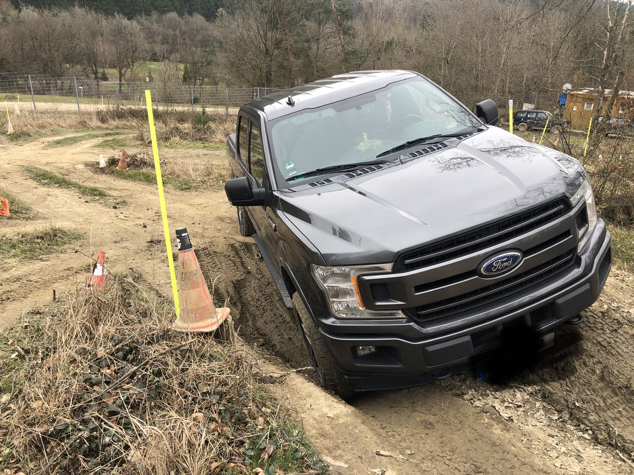 Ein Ford F-150 navigiert einen unebenen, matschigen Weg, umgeben von Verkehrshütchen und brauner Erde.
