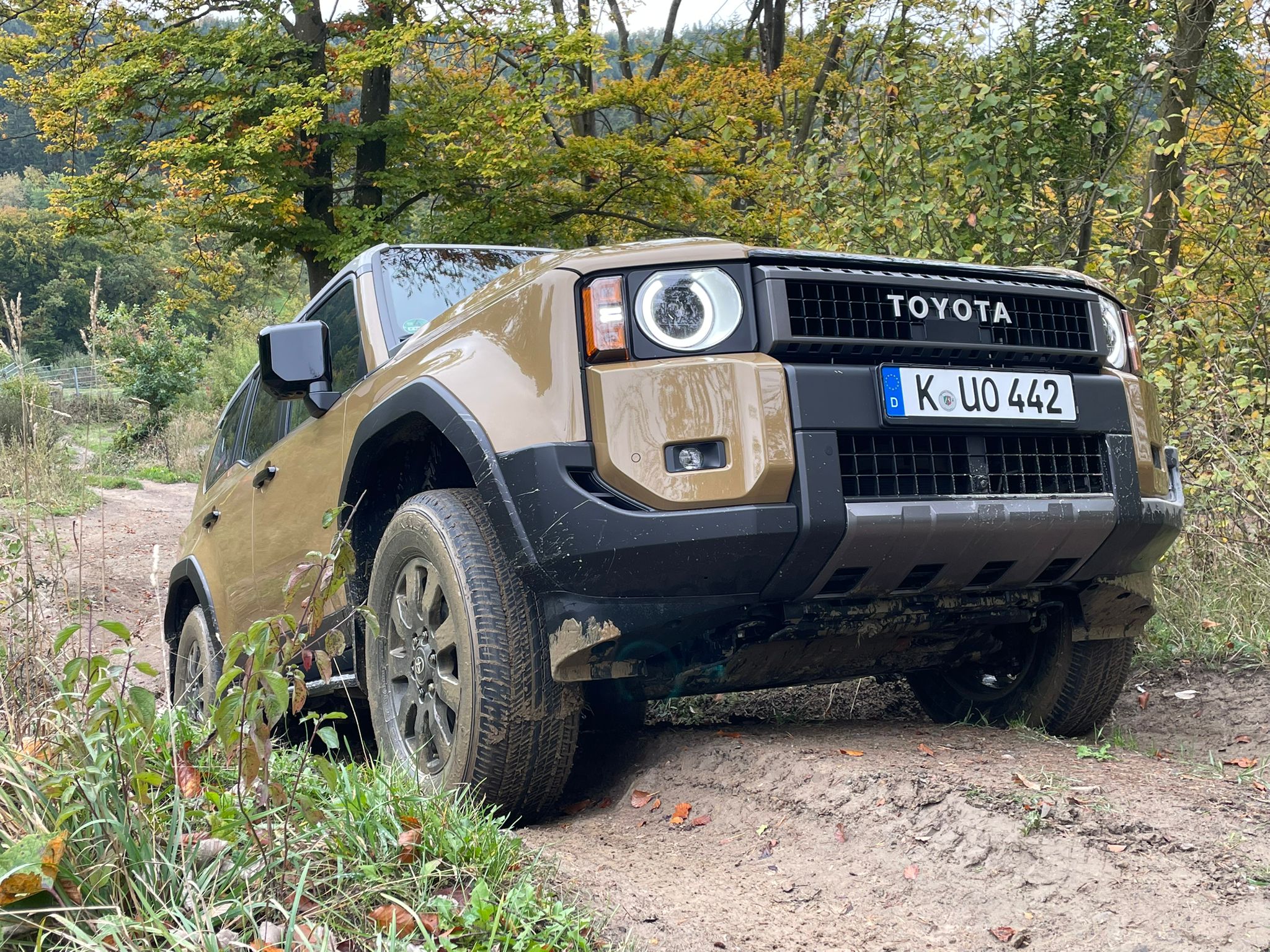 Ein Toyota Geländewagen fährt auf unbefestigtem Terrain umgeben von herbstlicher Natur.